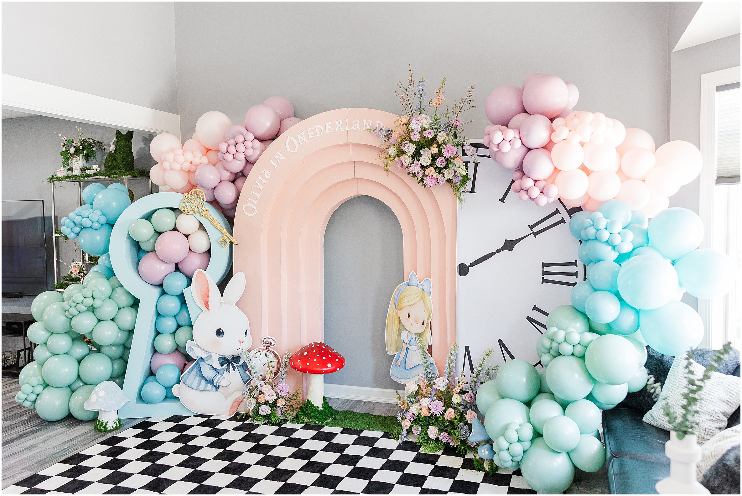 Alice in Wonderland themed backdrop with pastel balloons and large cut-outs at a first birthday party.