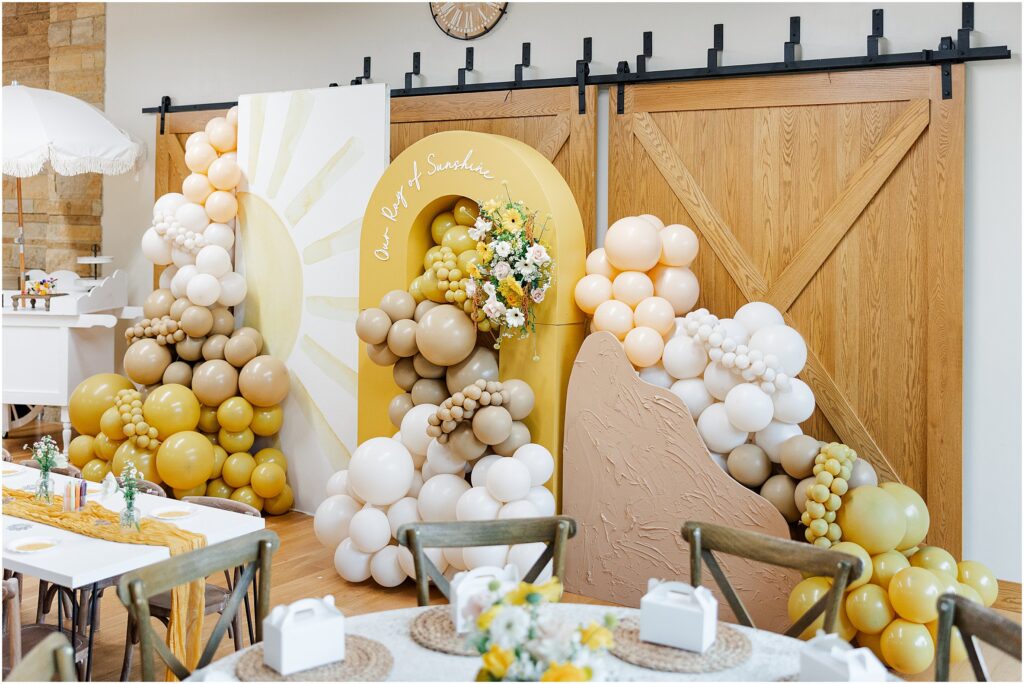 Sunny baby shower setup at Eagan Community Center with soft yellow tones, natural wood chairs, and floral arrangements in baskets.