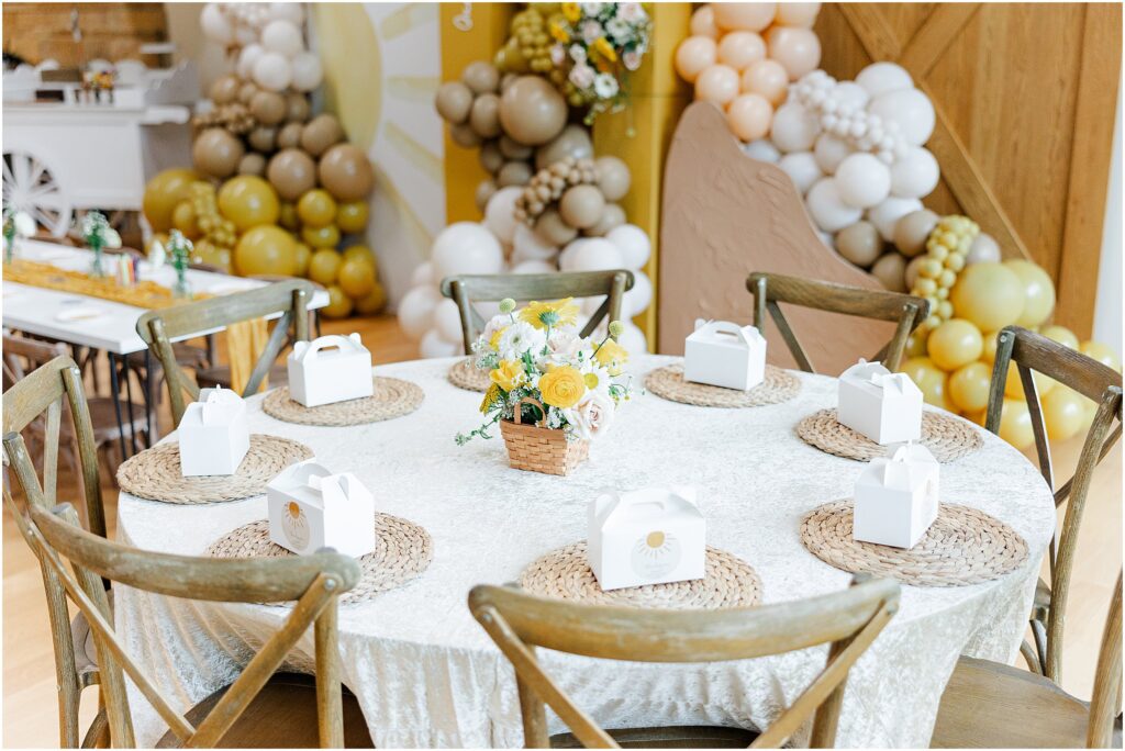 Sunny baby shower setup at Eagan Community Center with soft yellow tones, natural wood chairs, and floral arrangements in baskets.