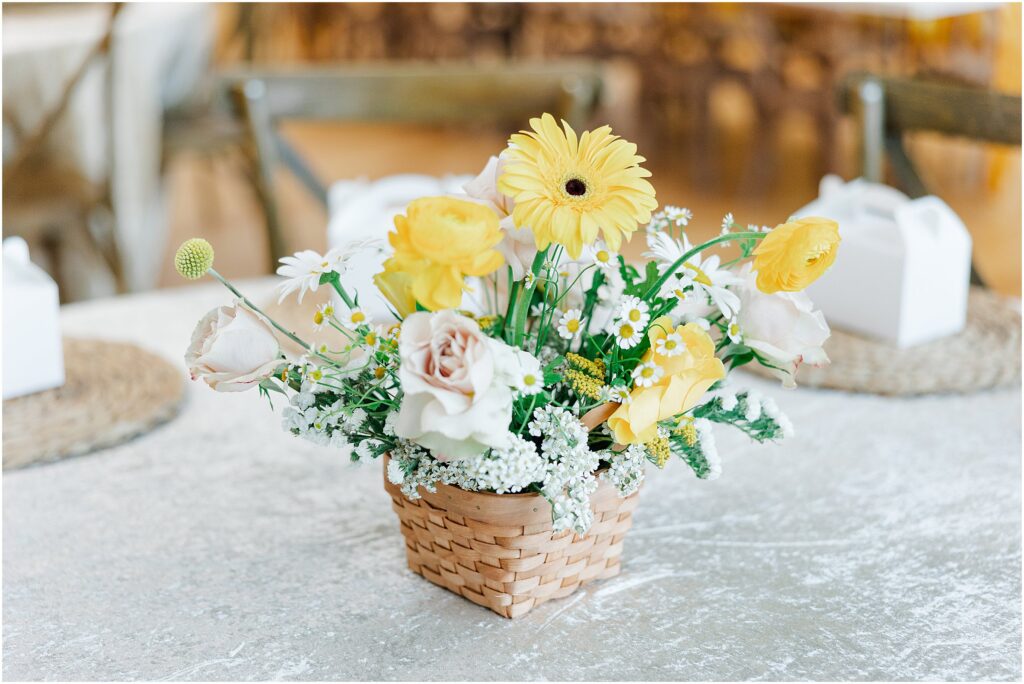 Sunny baby shower setup at Eagan Community Center with soft yellow tones, natural wood chairs, and floral arrangements in baskets.