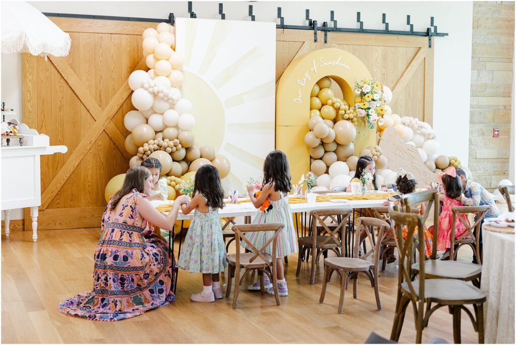 Sunny baby shower setup at Eagan Community Center with soft yellow tones, natural wood chairs, and floral arrangements in baskets.