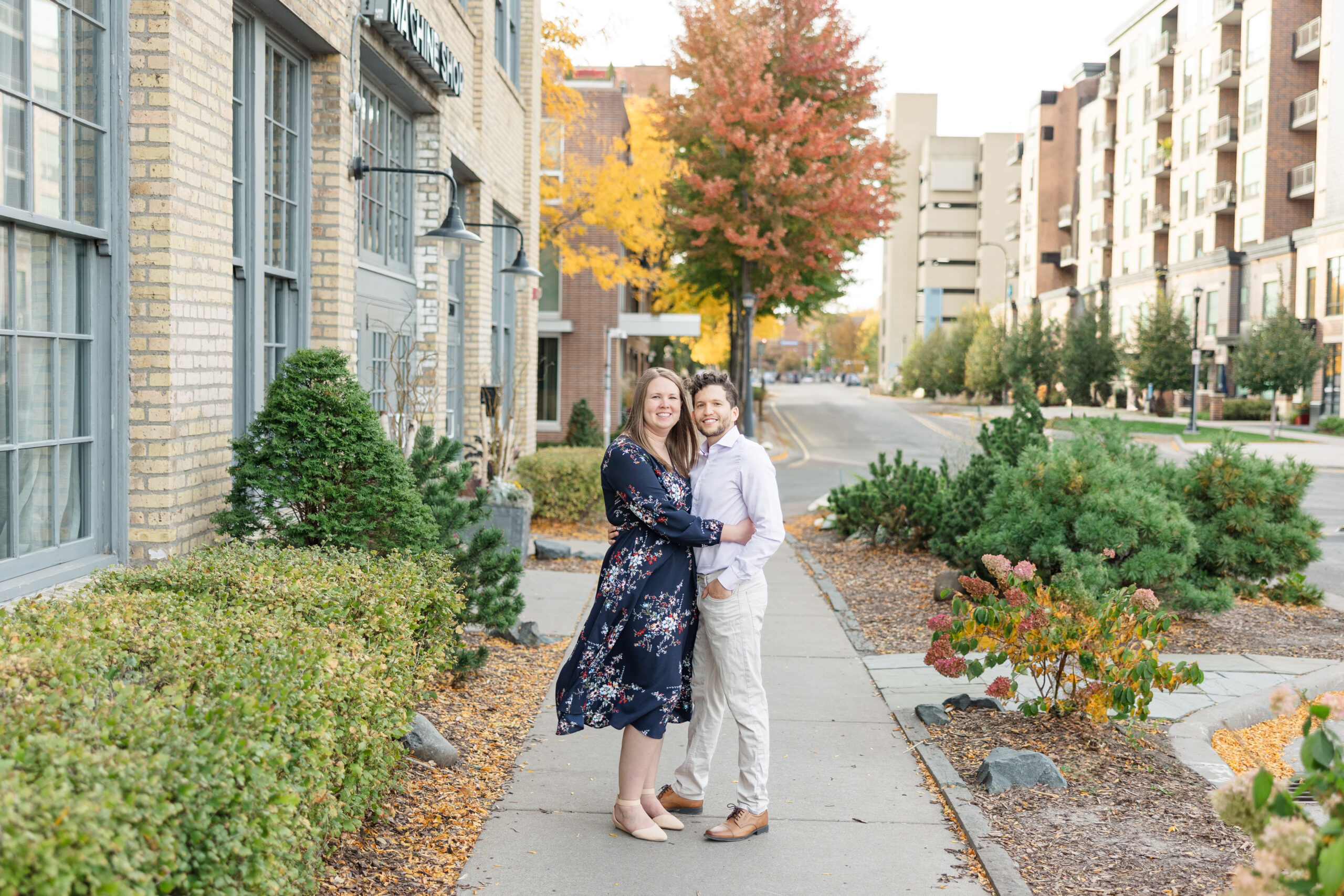 Engagement photo of Ashley and Gerardo outside Machine Shop Minneapolis, with an elegant urban backdrop and fall leaves.