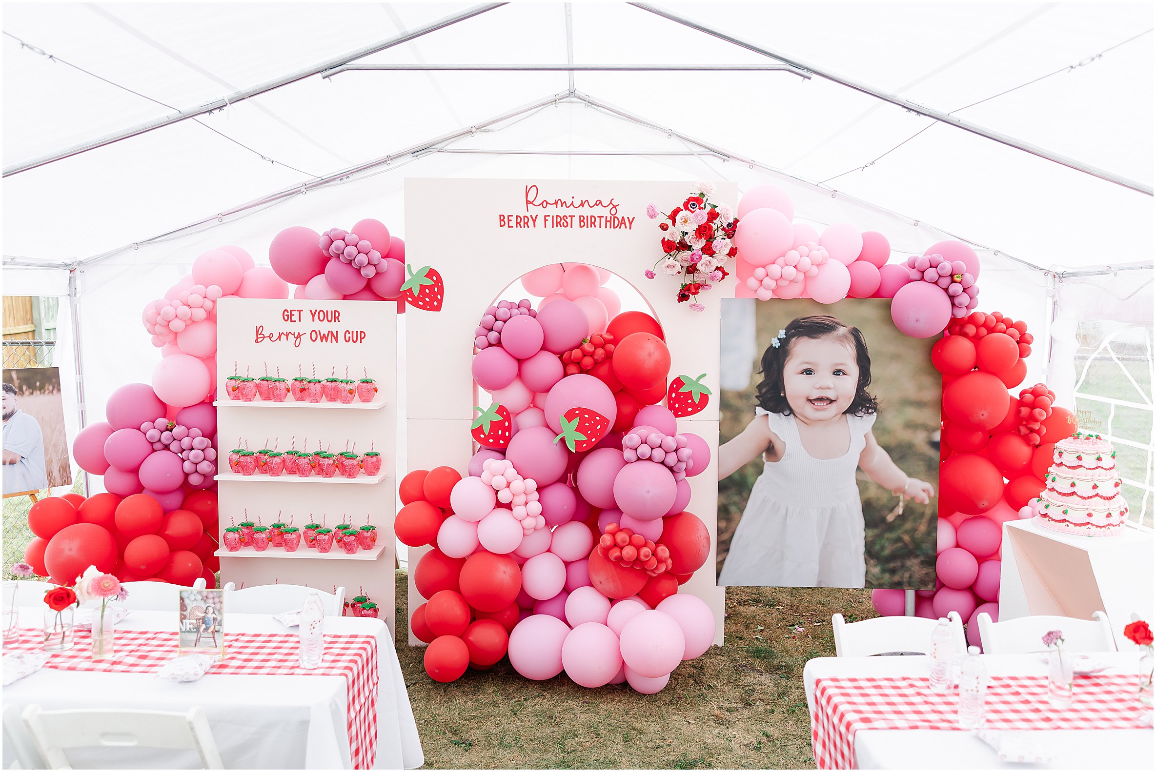 Romina’s Berry First Birthday Party with a strawberry-themed backdrop, red and pink balloons, florals, and a three-tiered strawberry cake.