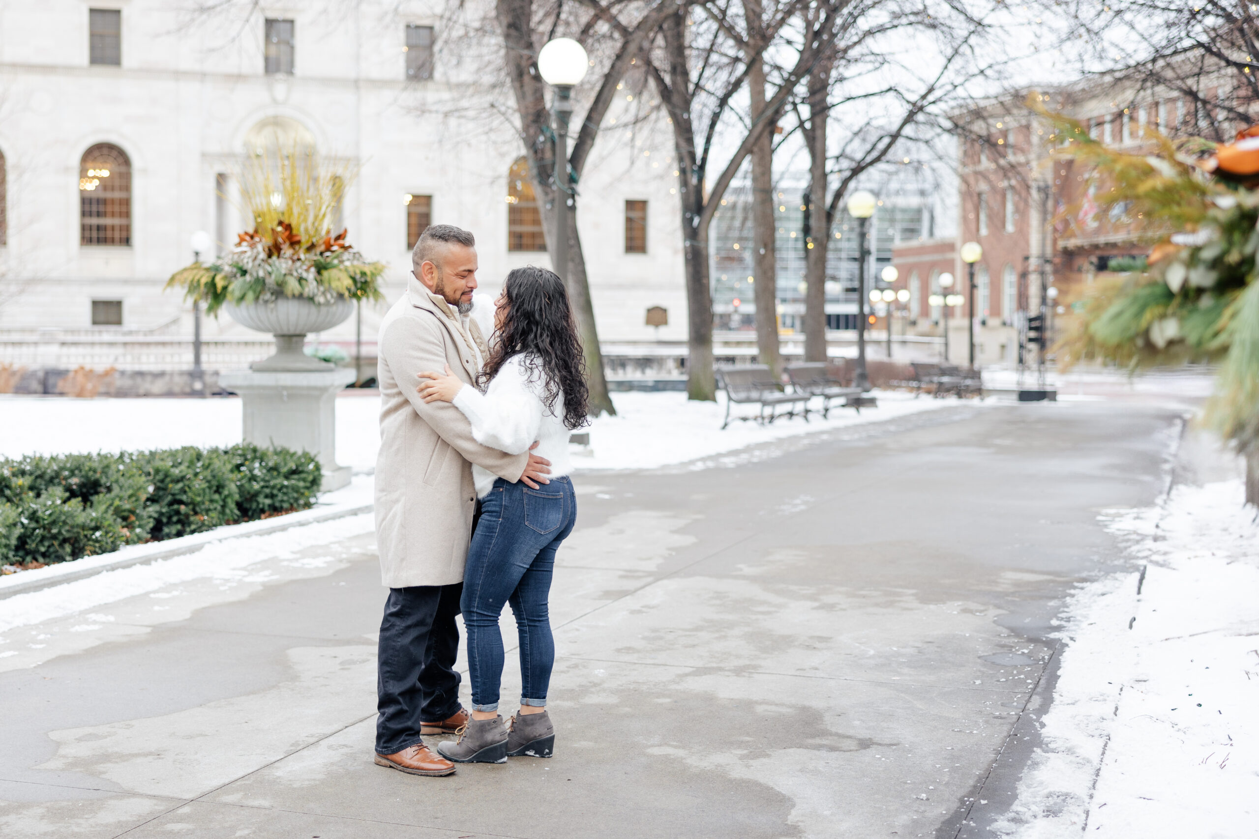 Couple embracing during a winter portrait session at Rice Park in St. Paul, with twinkling lights and fresh snow creating a romantic setting.